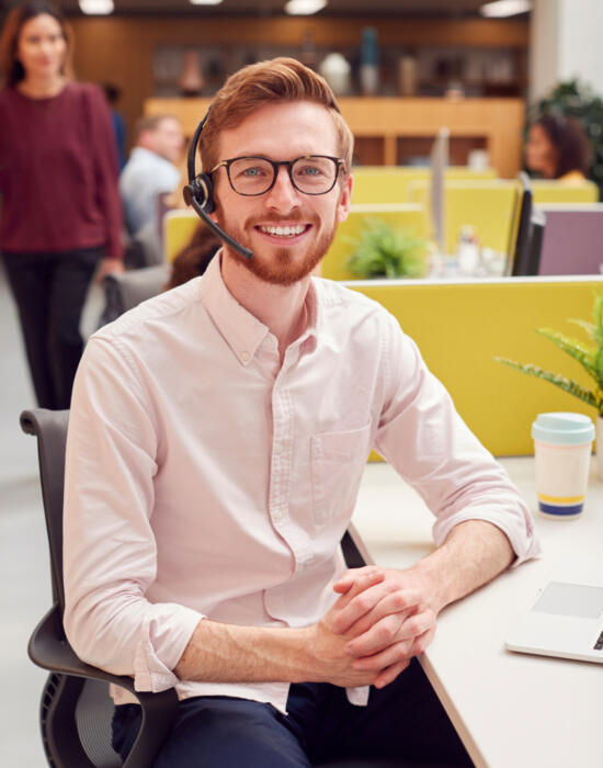 Portrait Of Businessman Wearing Headset Talking To Caller In Customer Services Centre