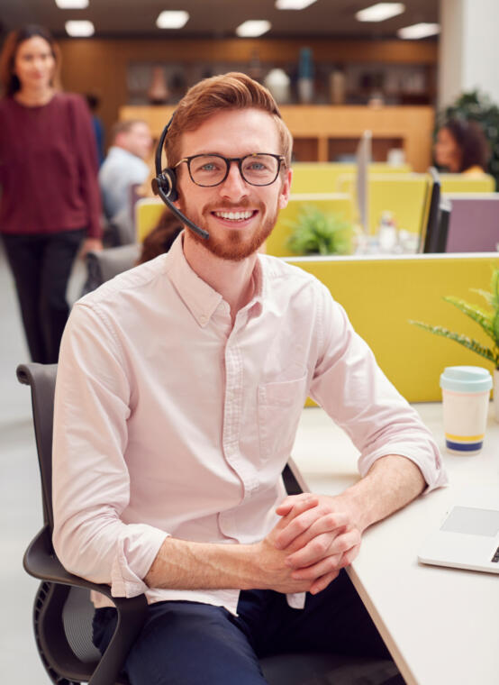Portrait Of Businessman Wearing Headset Talking To Caller In Customer Services Centre