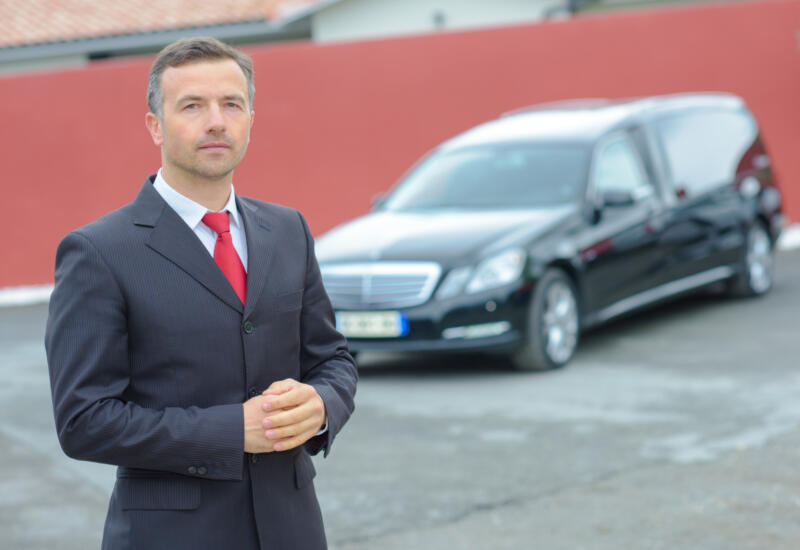 Funeral director with hearse in background