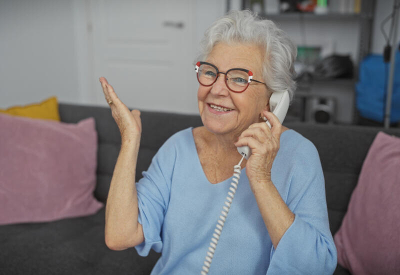 A cheerful senior woman in glasses speaking on a landline phone
